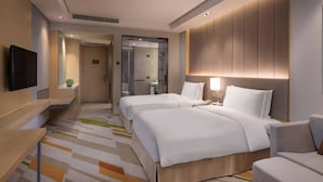 Ein Hotelzimmer mit zwei Betten, einem Fernseher, einem Schreibtisch und einer Dusche.