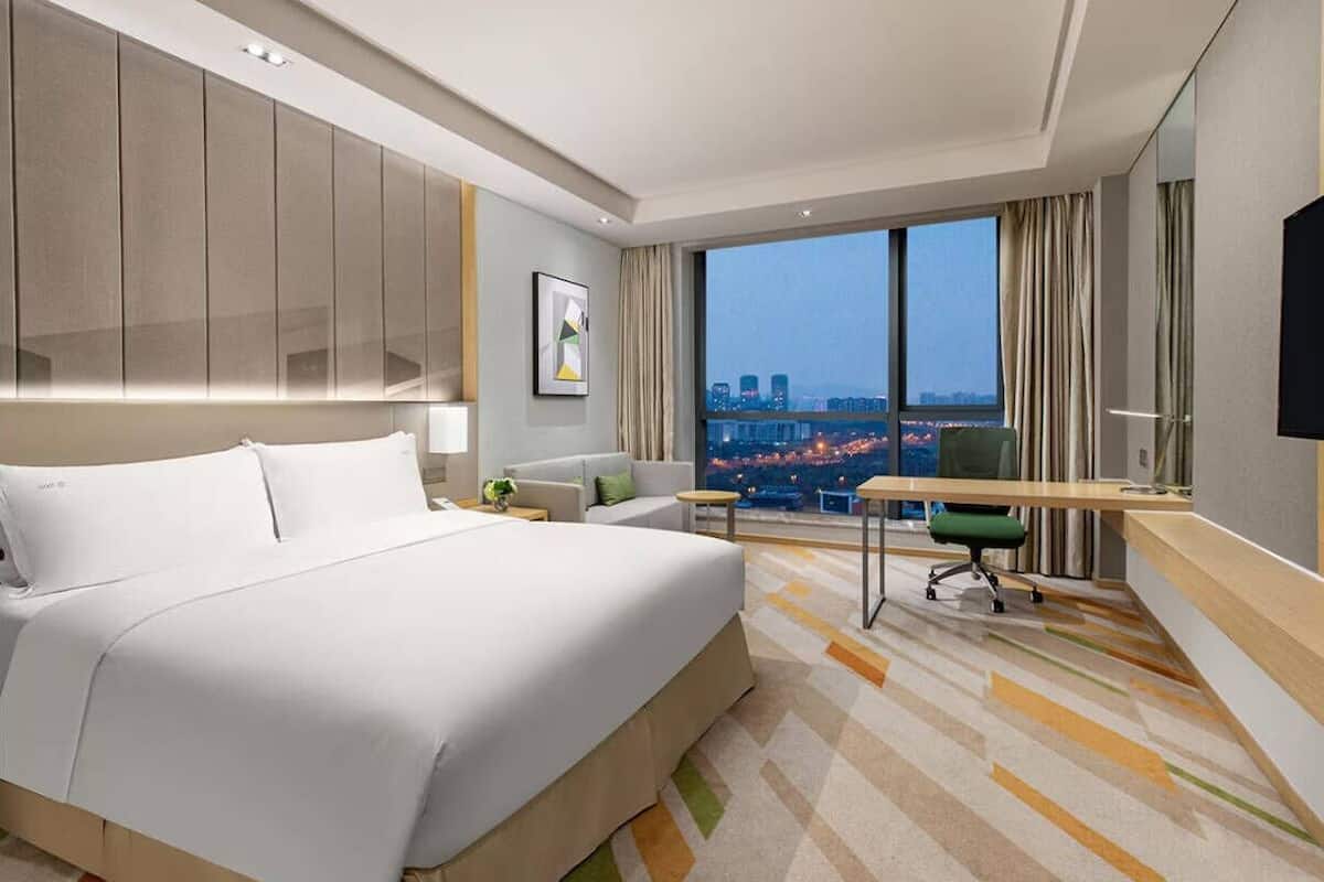Une chambre d’hôtel moderne dotée d’un grand lit, d’un bureau et offrant une vue sur le paysage urbain.