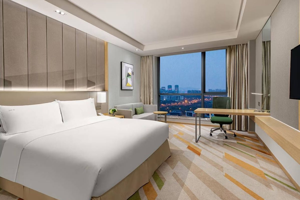 Une chambre d’hôtel moderne dotée d’un grand lit, d’un bureau et offrant une vue sur le paysage urbain.