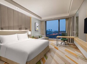 Ein modernes Hotelzimmer mit einem großen Bett, einem Schreibtisch und Blick auf die Stadt.