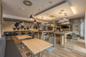 Een modern restaurant met houten tafels en grijze stoelen, geometrische wandmotieven en hanglampen.