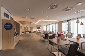 Un interior moderno con una mesa de recepción, varias zonas de estar y grandes ventanales que permiten la entrada de luz natural.