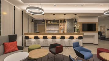 A modern hotel lobby with a bar area, seating arrangements, and a flat-screen TV.