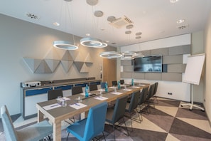 Una sala de conferencias moderna con una mesa larga, sillas, una pantalla de televisión y luces en el techo.