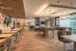 A modern restaurant interior with wooden flooring, multiple seating areas, and pendant lighting. - Holiday Inn Express Wuppertal - Hauptbahnhof by IHG (Wuppertal)