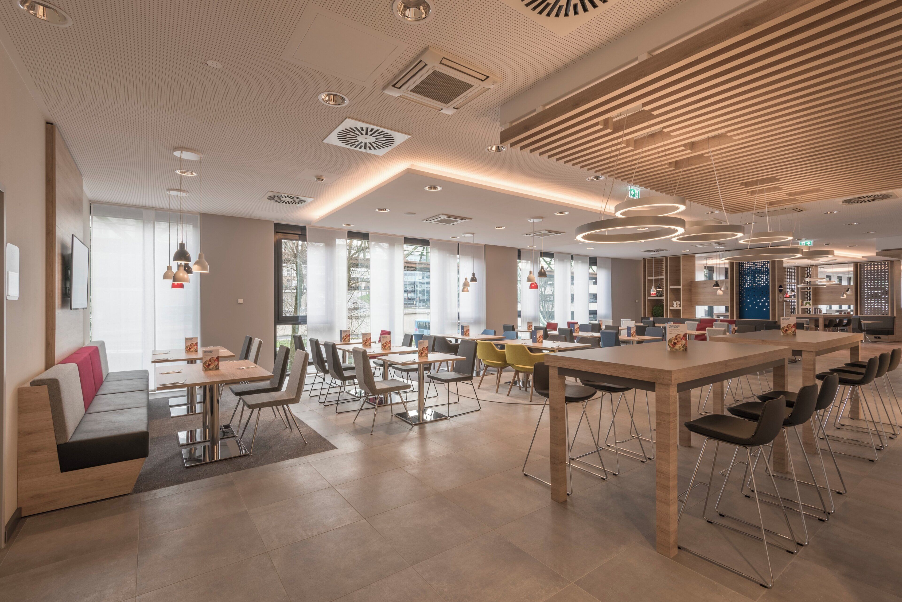 A modern dining area with high tables and chairs, large windows, and a ceiling with a unique pattern.