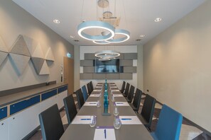 Una sala de conferències amb una taula llarga, cadires i lluminàries modernes.