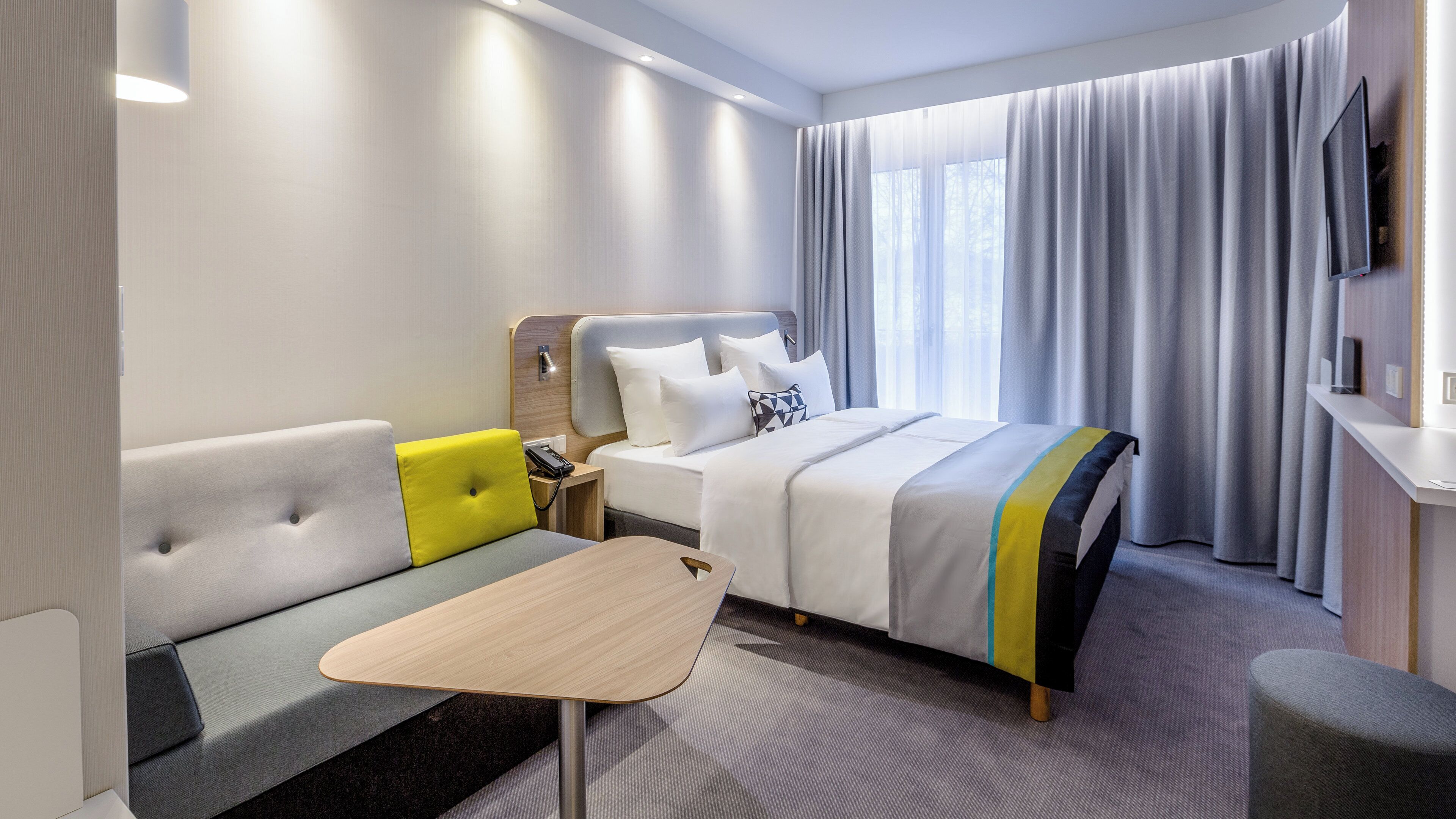 Ein Hotelzimmer mit Bett, Sofa, kleinem Tisch und Fernseher.