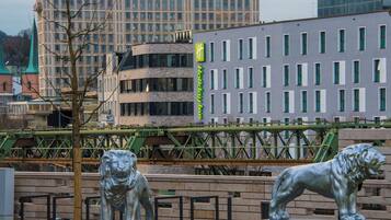En staty av ett lejon på ett offentligt torg, med moderna byggnader i bakgrunden.