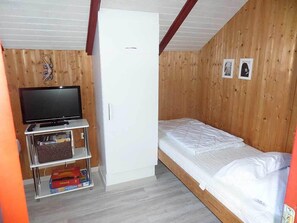 A small, wooden-paneled room with a single bed, a television on a stand, and a white wardrobe. - Juwel Feriendorf-Reihenhaus Blaue Blume (Gluecksburg)