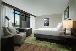 A hotel room with a bed, a TV, a chair, a desk, a lamp, and a window with curtains. - Hilton Garden Inn Memphis Downtown Beale Street (Memphis)