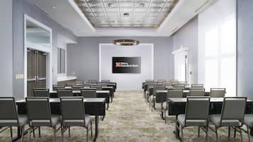 A conference room with a large screen displaying the Hilton Garden Inn logo, arranged seating, and a patterned carpet.