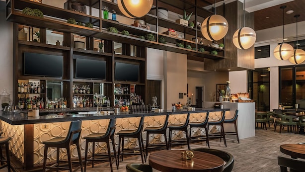 A bar area with a long counter, multiple bar stools, and a variety of bottles and glasses. - Hilton Garden Inn Memphis Downtown Beale Street (Memphis)
