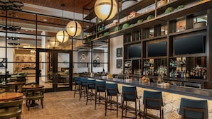A modern bar area with a long counter, multiple bar stools, and a variety of bottles and glasses on shelves. - Hilton Garden Inn Memphis Downtown Beale Street (Memphis)