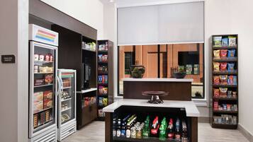 Uma despensa moderna de hotel com prateleiras para lanches refrigerados e não refrigerados, um refrigerador de bebidas e uma área de estar com vista.