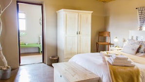 Une chambre avec un lit en bois, une armoire blanche, un banc en bois et une vue sur un banc vert à l’extérieur.