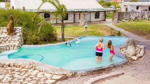 Une piscine bordée de pierres, une statue et une maison en arrière-plan.