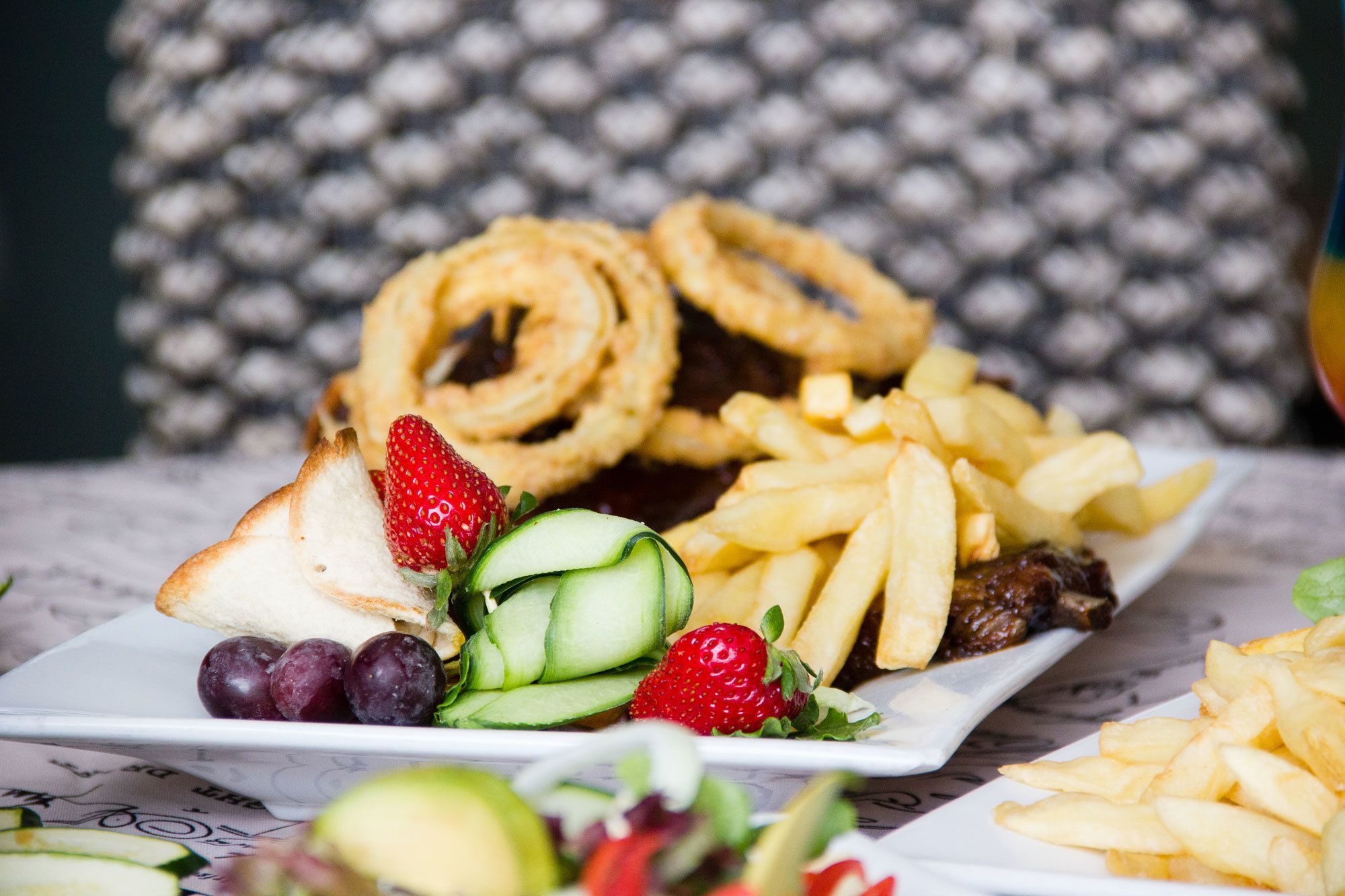 Une assiette de nourriture comprenant des oignons frits, des frites et une salade aux fraises et aux concombres.
