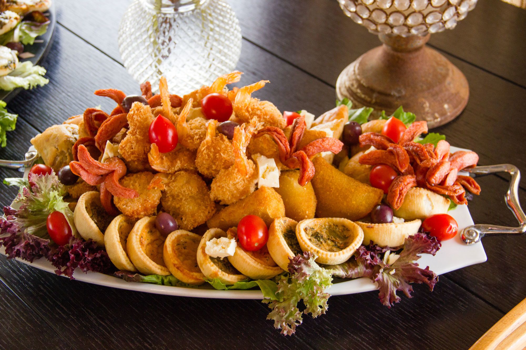 A platter of assorted appetizers including fried shrimp, olives, and various vegetables.