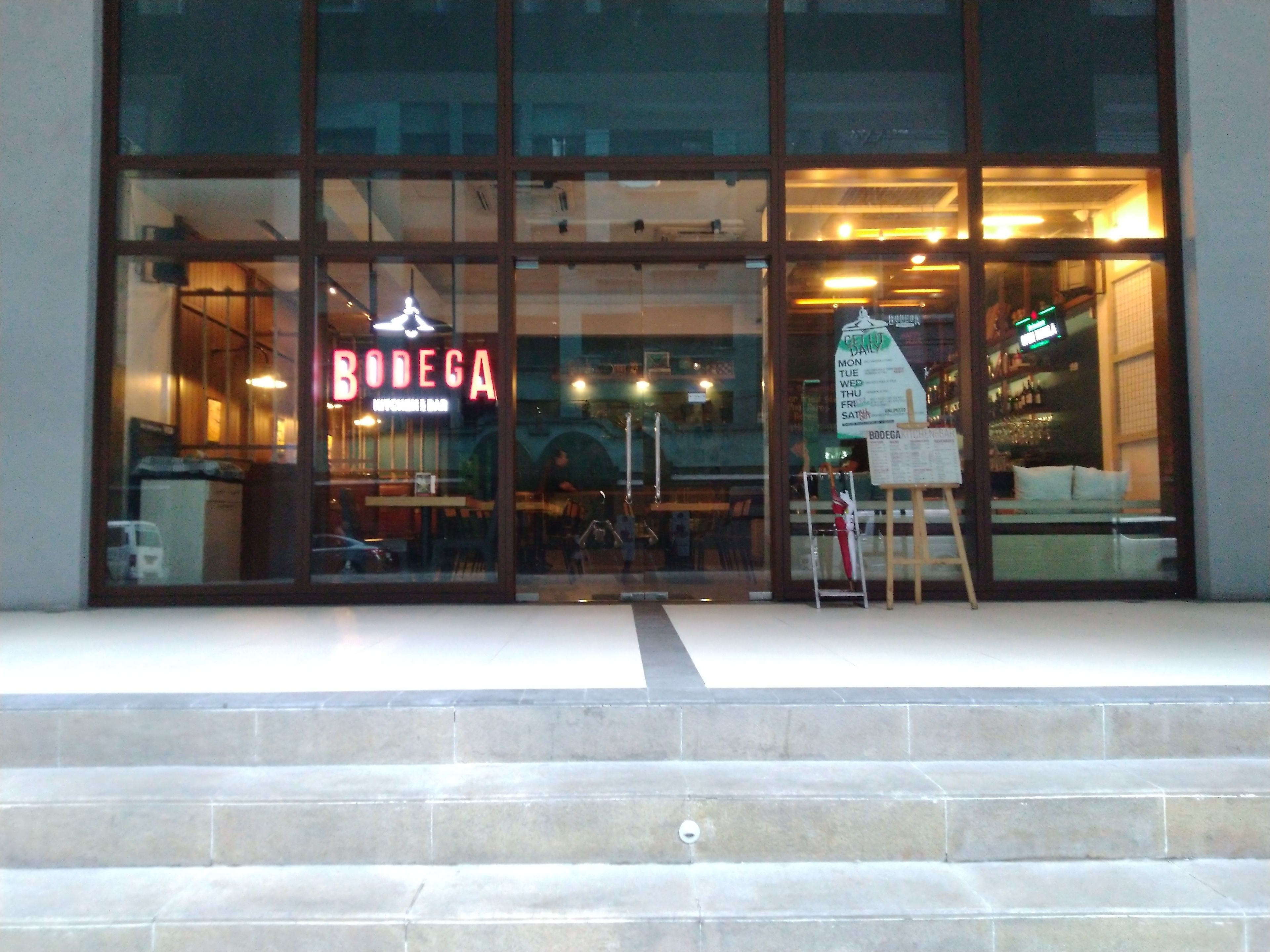 A restaurant with a glass facade and a neon sign reading "BODEGA".
