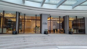 A modern hotel entrance with glass doors, a reception desk, and a staircase leading up. - Three Central (Makati)