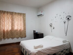 Un dormitorio con cama, escritorio y silla. Hay una ventana con cortinas, un aire acondicionado en la pared y un cuadro de diente de león.
