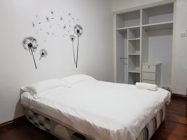 Una cama bien hecha con ropa blanca, un armario blanco con varios estantes y una decoración en la pared hecha con semillas de diente de león.