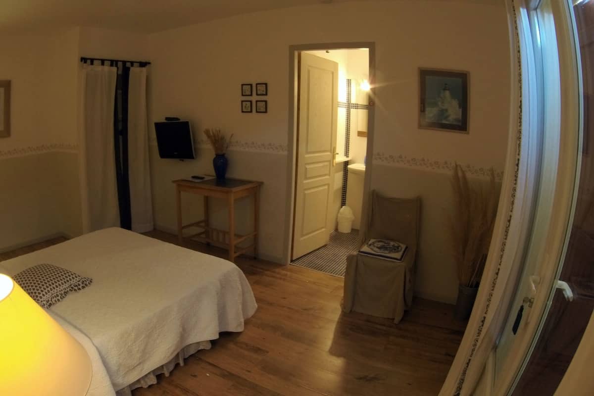 A bedroom with a bed, bedside lamps, a small table with a vase, a television, and a door leading to a bathroom.