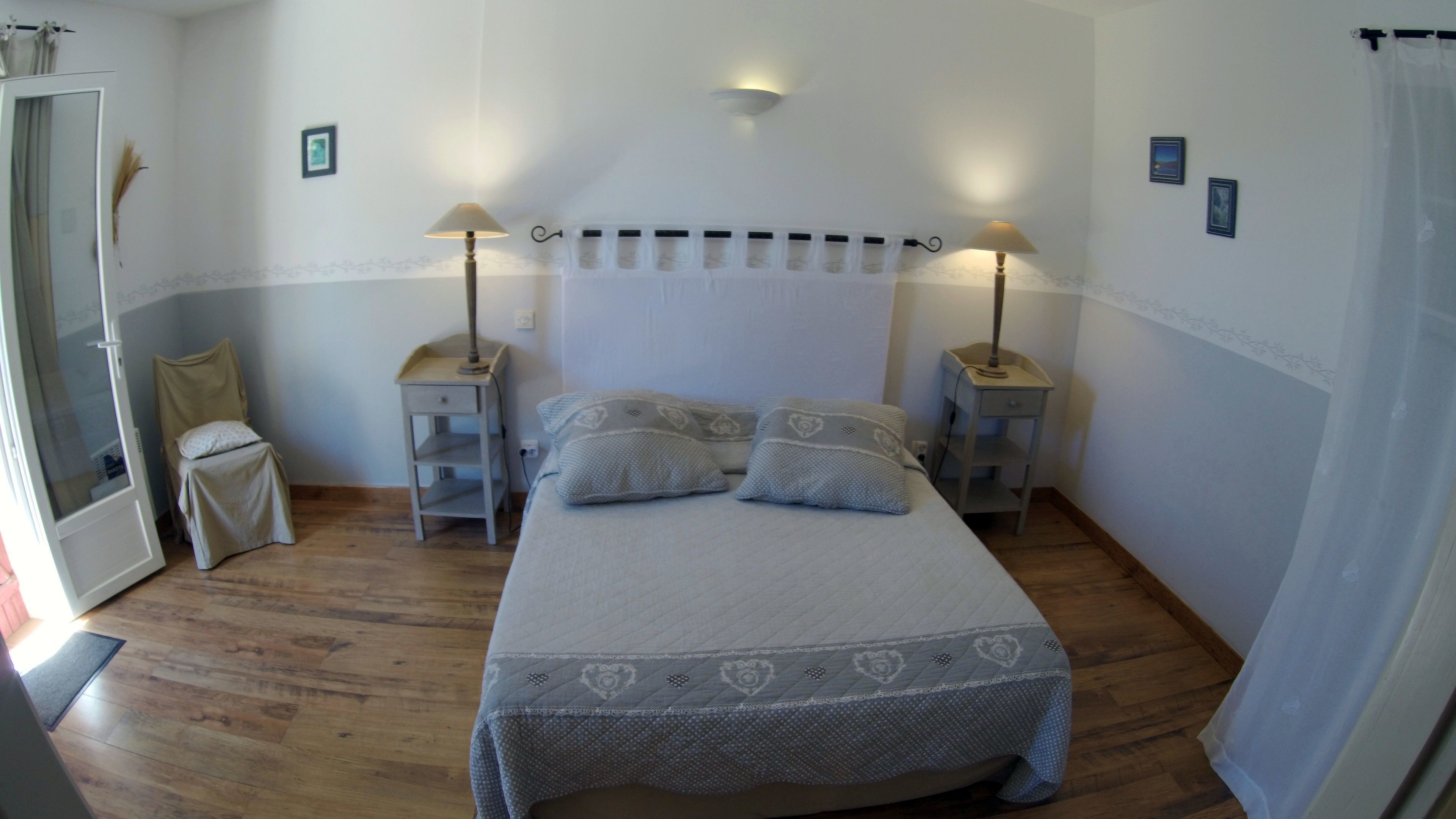 Un dormitorio con una cama, dos mesitas de noche, una mesita auxiliar, una puerta y una ventana.