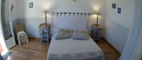 Un dormitorio con una cama, dos mesitas de noche, una mesita auxiliar, una puerta y una ventana.