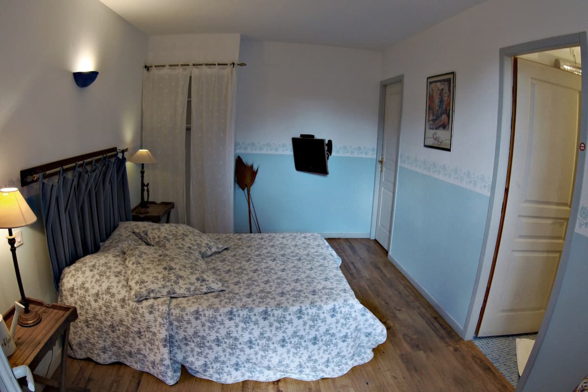 A bedroom with a bed, a nightstand, a lamp, a door, and a wall-mounted picture.