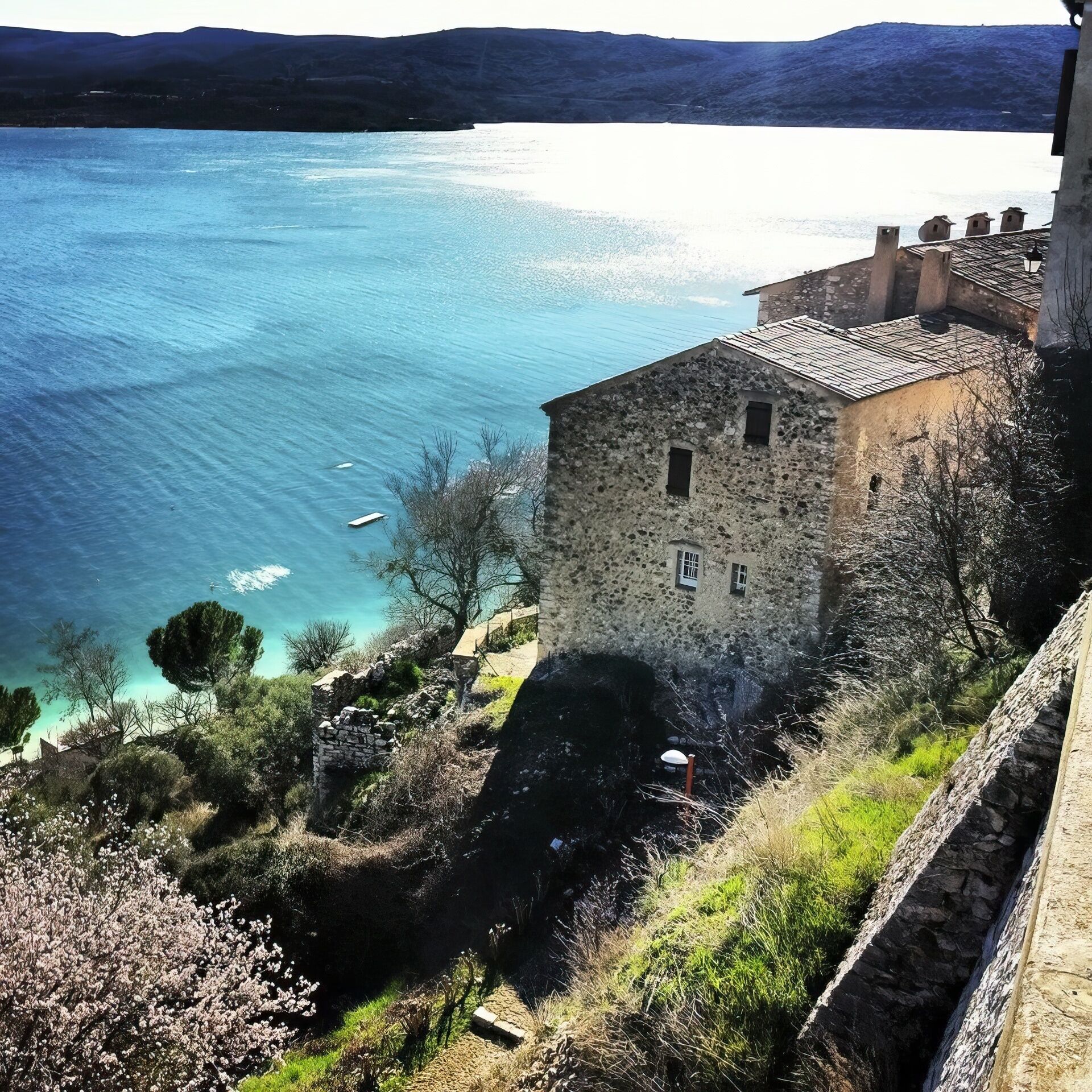 Un edificio de piedra con tejado de tejas que da a un lago azul y despejado.