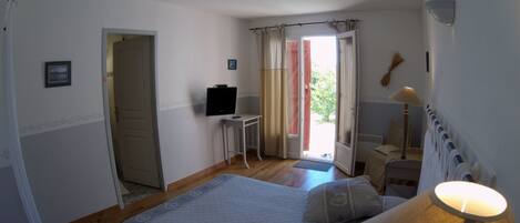 Un dormitorio con cama, escritorio, televisión y ventana con cortinas.