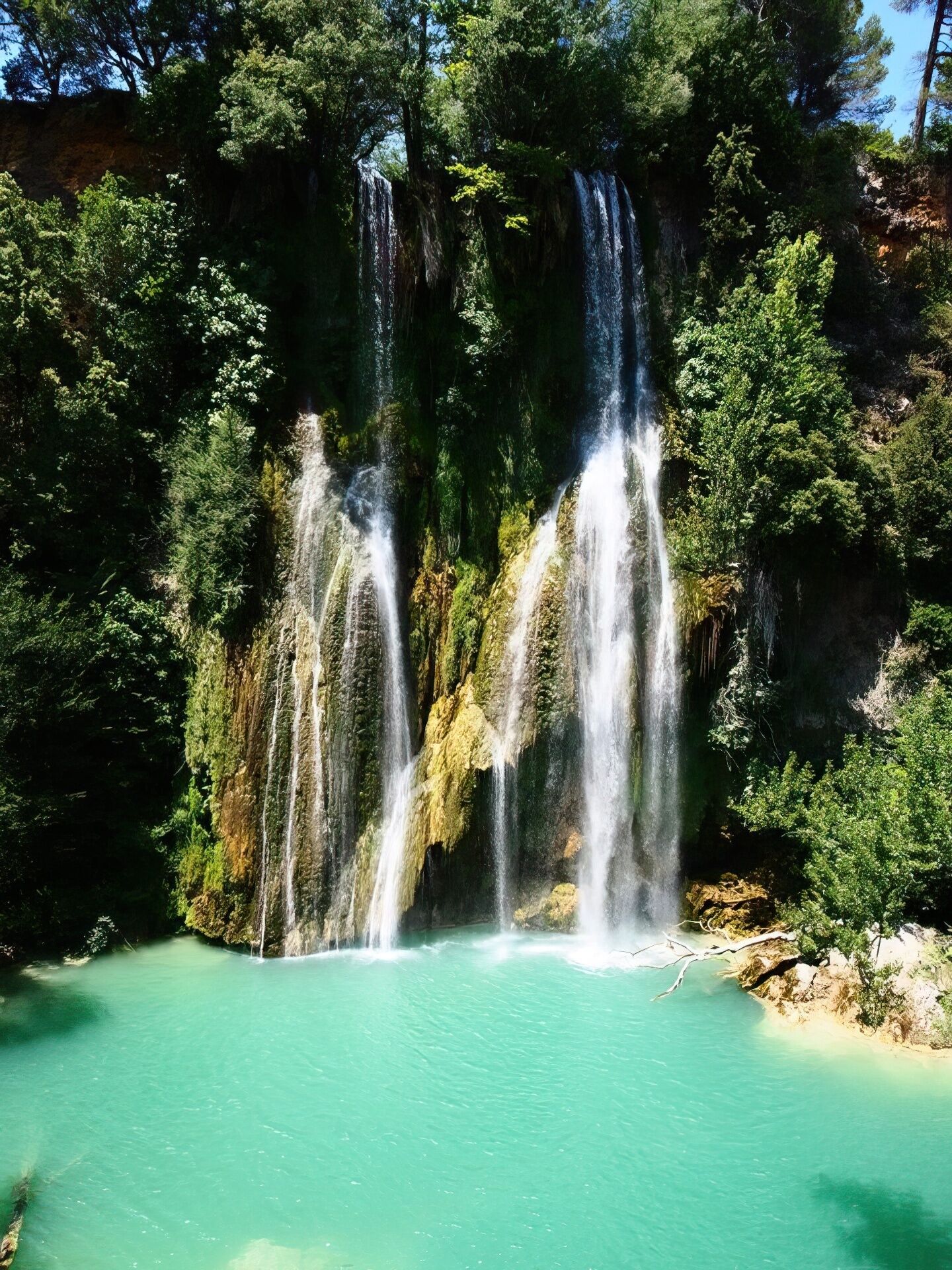 A waterfall cascading into a turquoise pool surrounded by dense greenery.