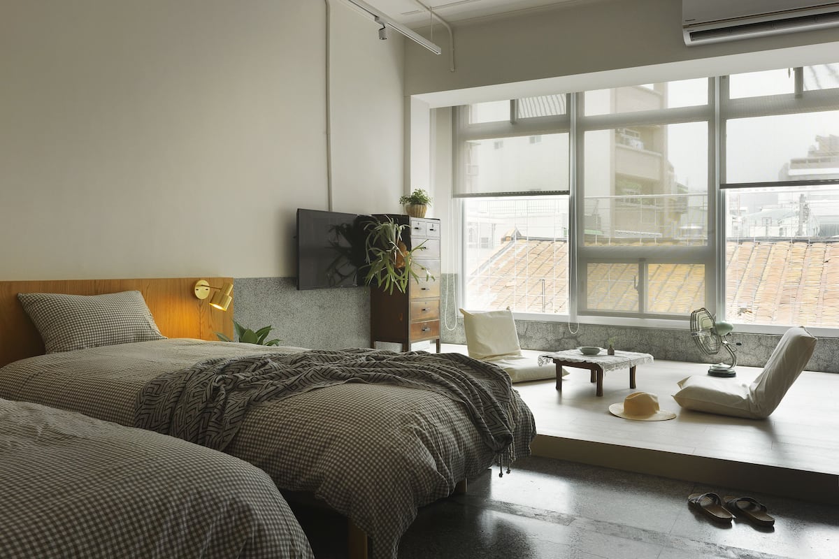 A modern bedroom with a large bed, a desk, a chair, and a view of the city through large windows.
