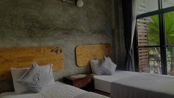 Quarto com duas camas, cada uma com cabeceira de madeira e roupa de cama branca. Há uma pequena mesa de cabeceira de madeira entre as camas, e uma luminária fixada na parede acima delas.