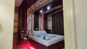 Quarto com cama, mesa de cabeceira, telefone e janela com cortinas.