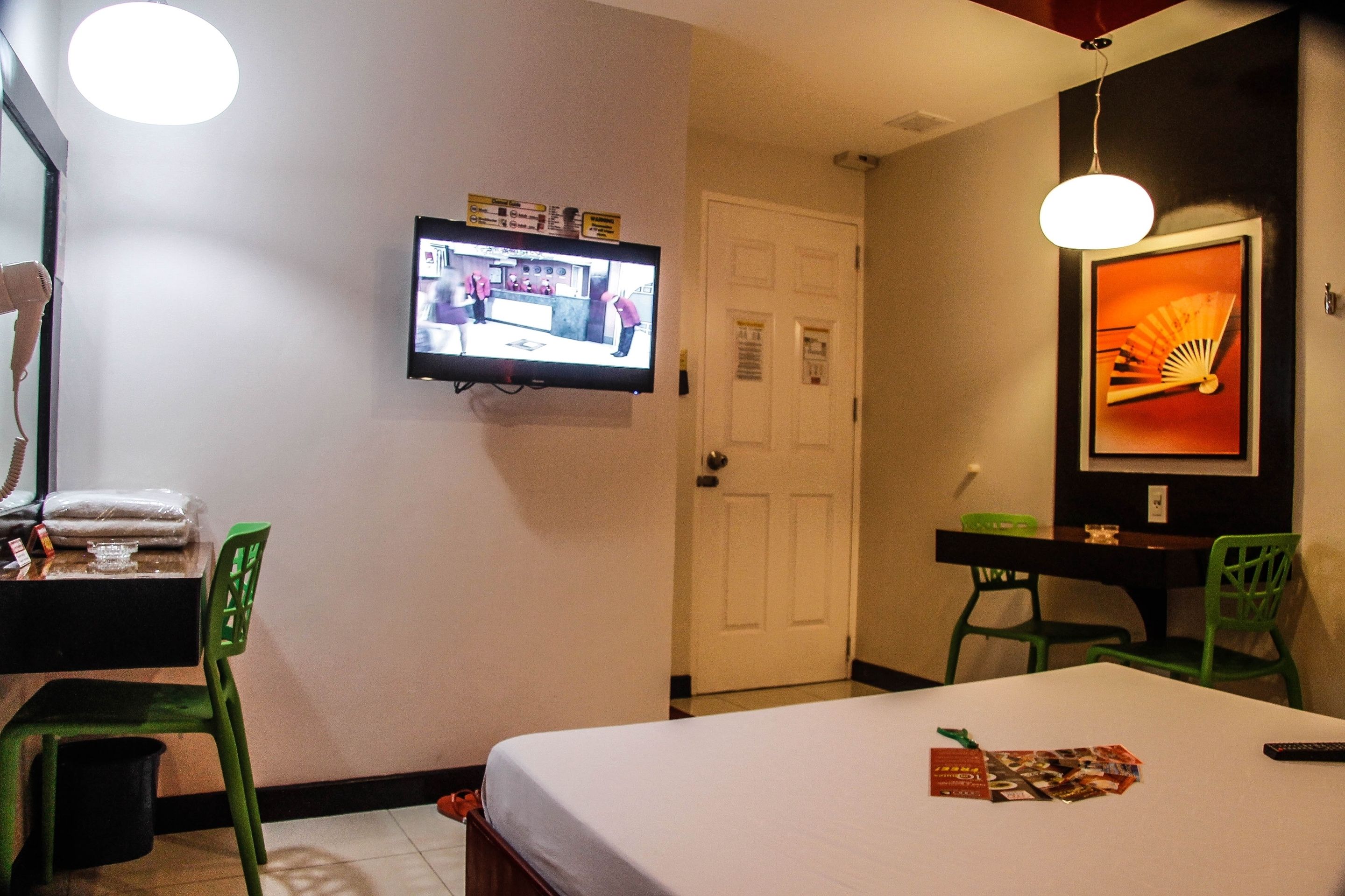 Een hotelkamer met een bed, een aan de muur bevestigde televisie, een groene stoel, een klein tafeltje en een deur.