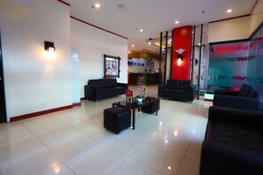 Eine moderne Hotellobby mit schwarzen Sofas, einem Empfangstresen und einer Glaswand mit Kunstwerken.