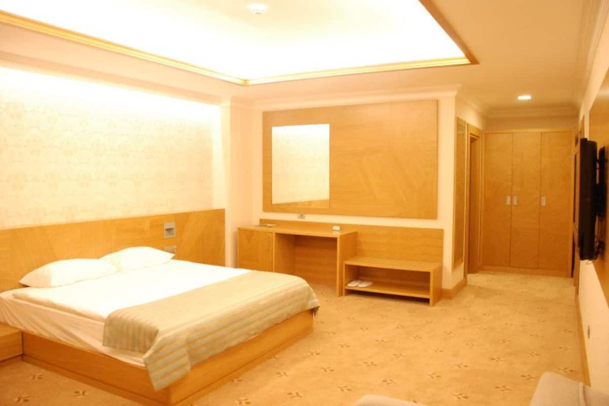 A hotel room with a bed, a wooden wardrobe, a mirror, and a television.
