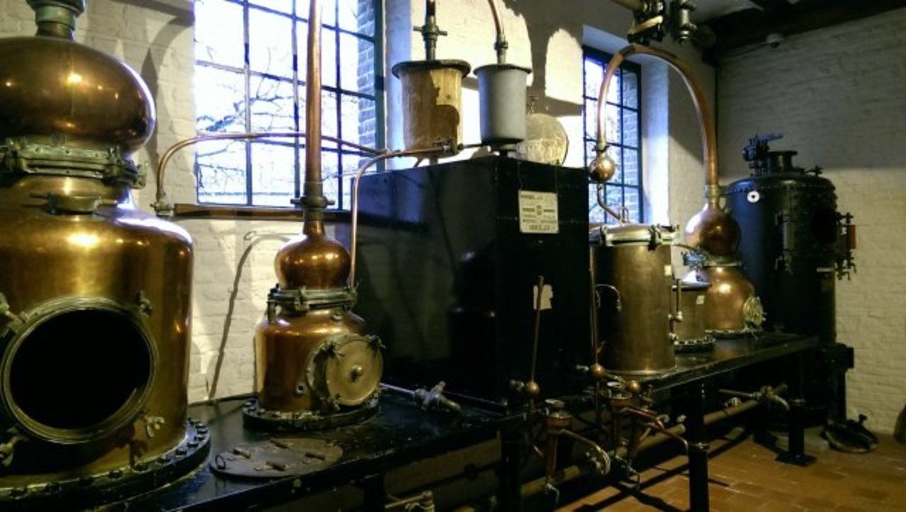 A vintage laboratory with brass distillation apparatus, a large black machine, and copper tanks.