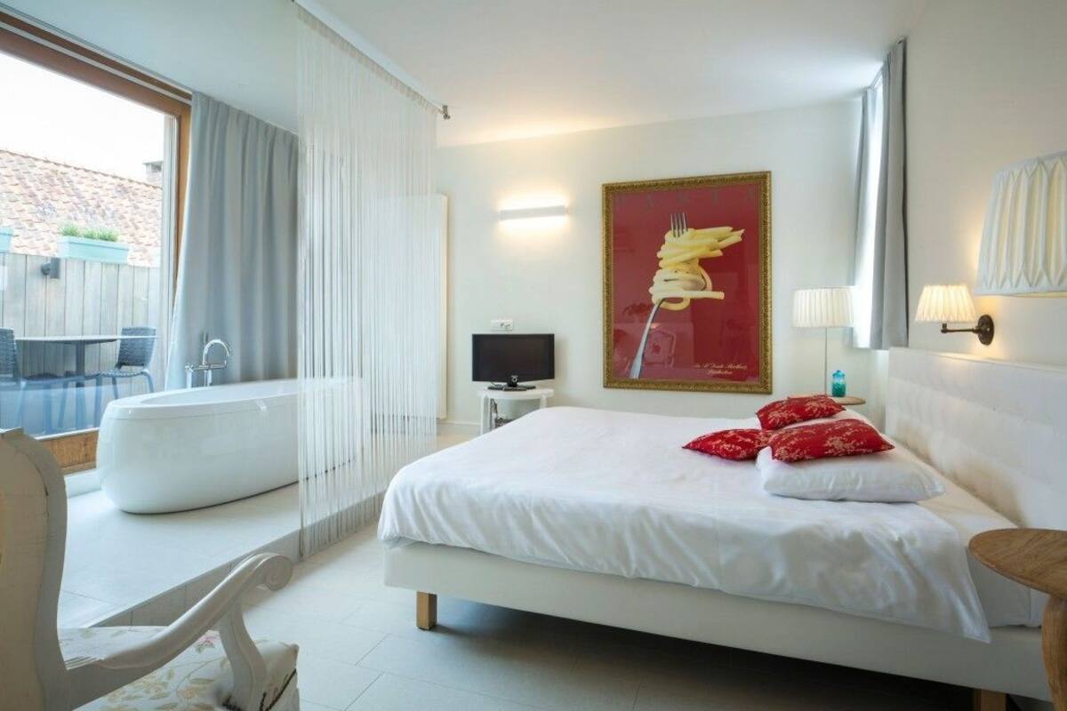 A modern hotel room with a large bed, a sitting area with a chair and a small table, a bathtub, and a television.