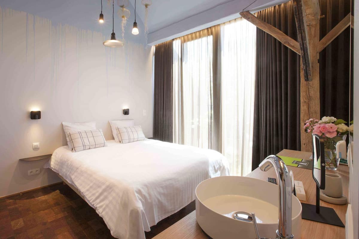 A modern hotel room with a large bed, a round sink, and a wooden ceiling beam.