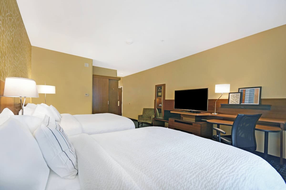 Een hotelkamer met twee bedden, een bureau, een stoel, een televisie en een bureaulamp.