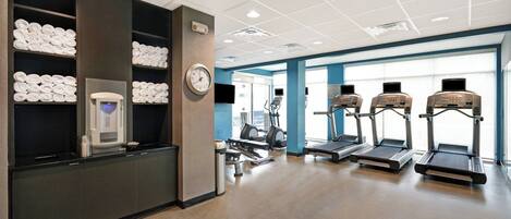A gym with exercise equipment, towels, and a clock.