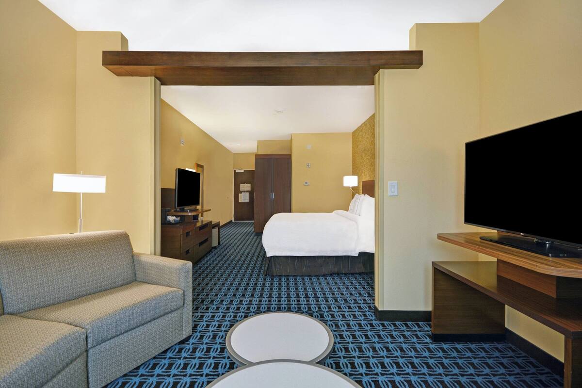 Een hotelkamer met een bank, een bed, een televisie, een bureau en een kamerbreed tapijt met een patroon.