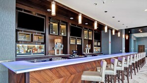 A long bar area with multiple shelves displaying bottles and glasses, a counter with a digital screen, and several bar stools.