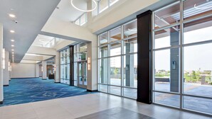 A spacious lobby with a blue carpet, large windows, and a high ceiling with circular light fixtures.