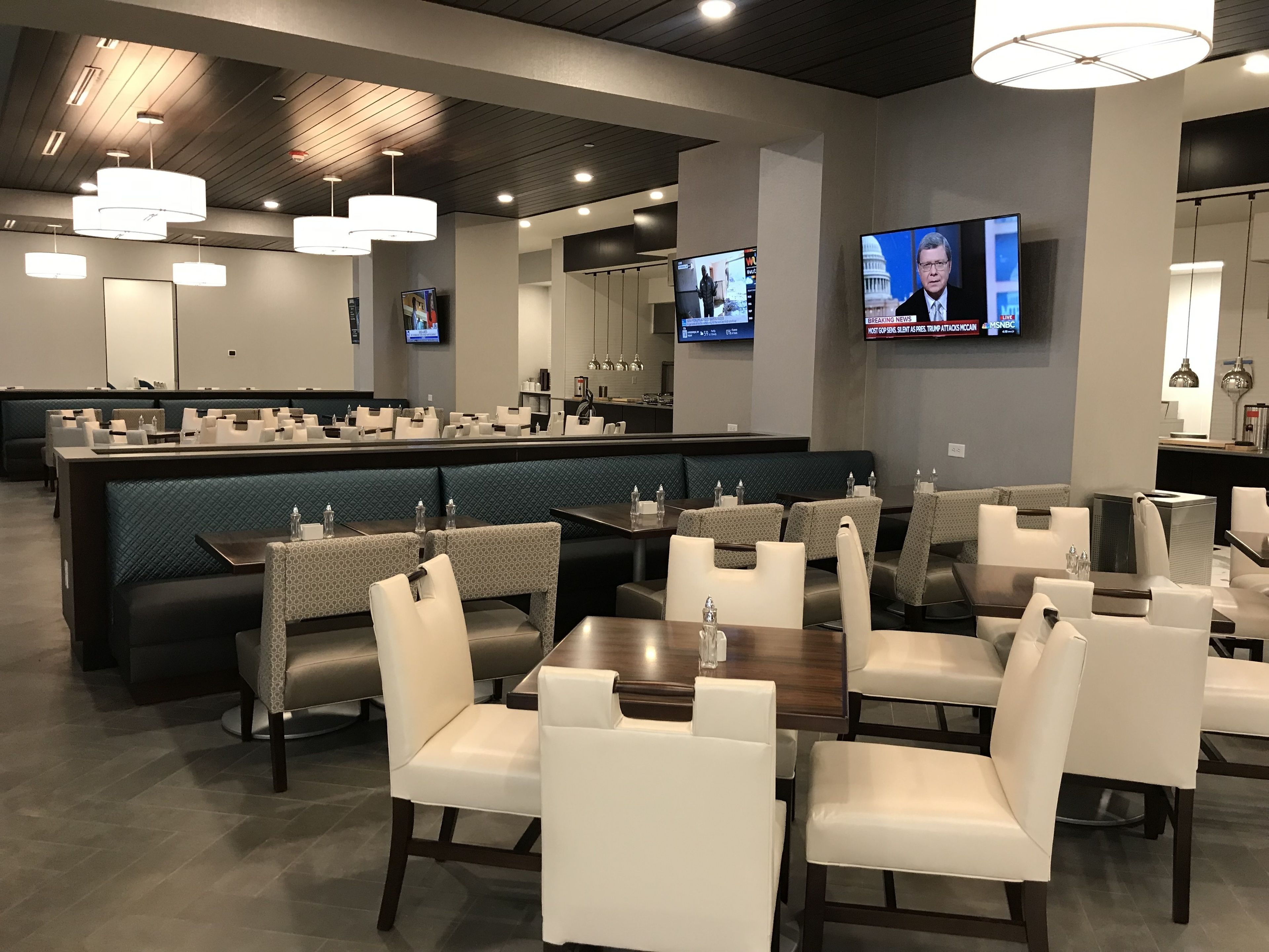 A modern restaurant with a bar area, multiple seating options including booths and tables, and televisions displaying news.