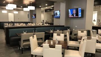 A modern restaurant with a bar area, multiple seating options including booths and tables, and televisions displaying news.